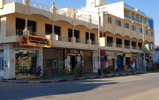 Eine Straße in Hurghada, Ägypten. Es ist ein Häuserblock mit verschiedenen Geschäften sichtbar.
